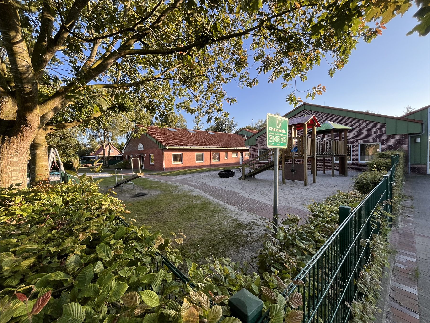 Außengelände des Kindergartens Neuschoo mit Spielgeräten und altem Baumbestand